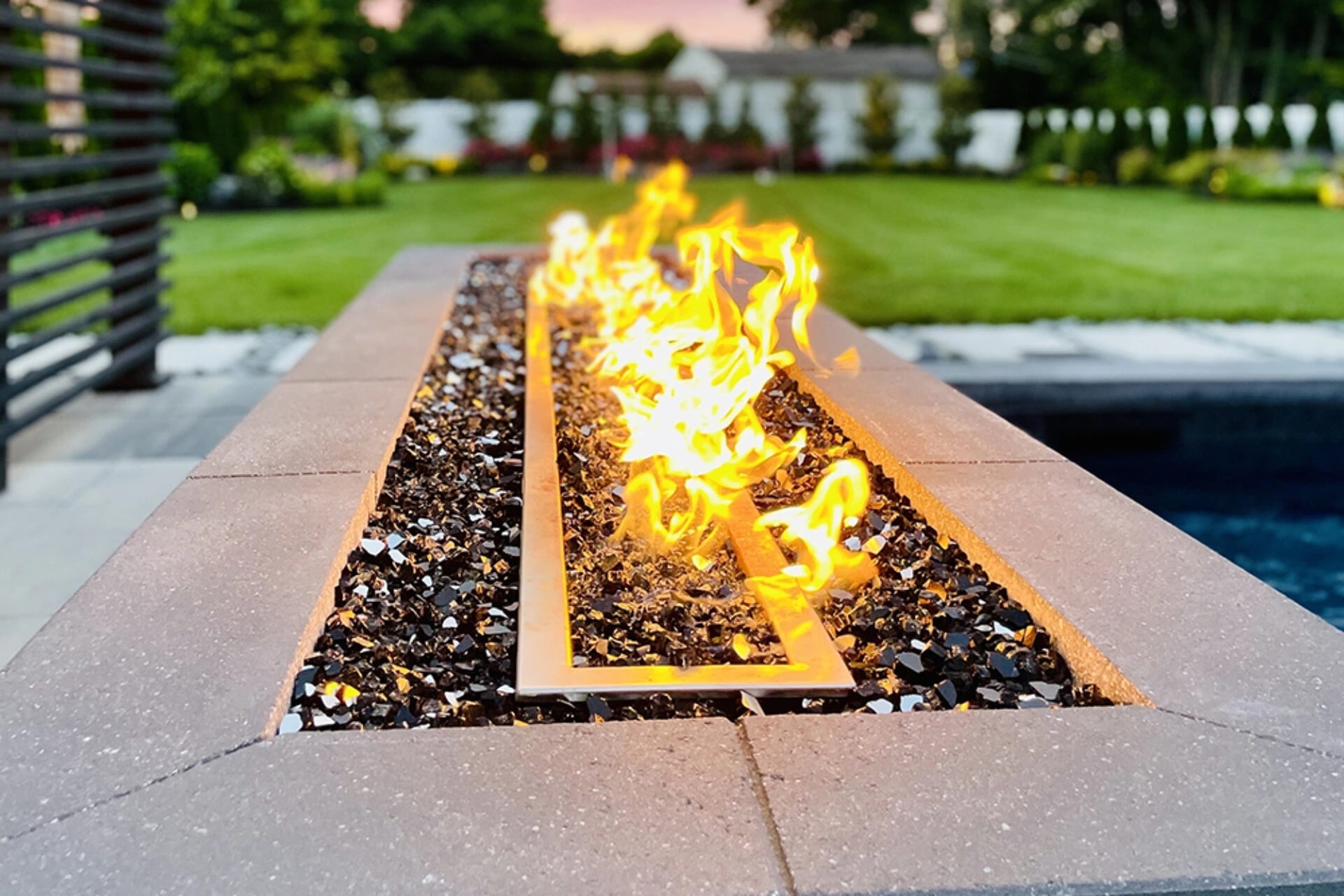 Lit rectangular fire pit beside a garden lawn