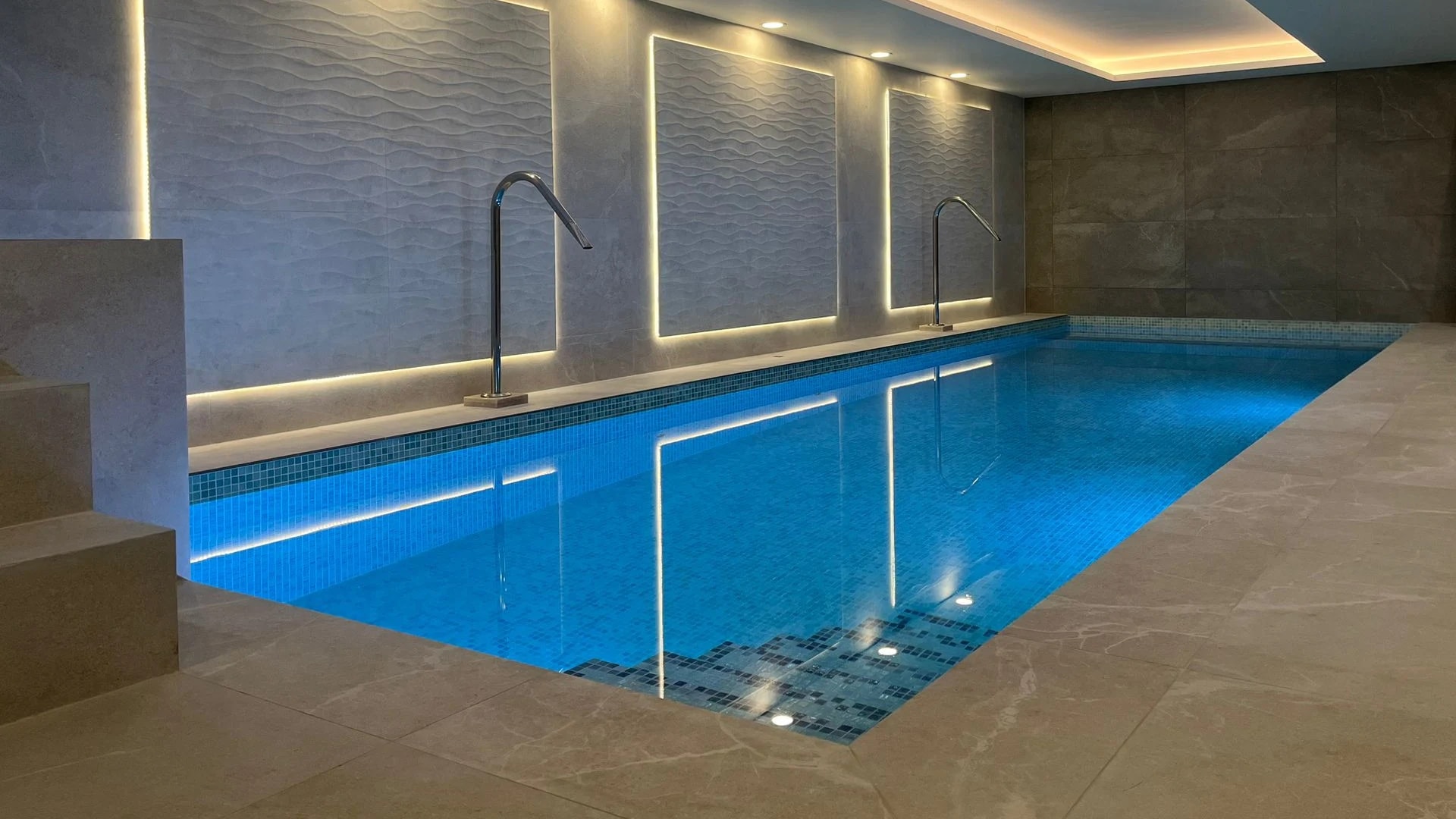 Indoor swimming pool with vivid blue mosaic tiles, sculpted stone walls and warm architectural lighting
